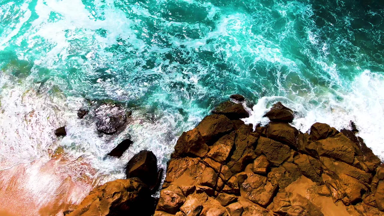 Overhead view of surf curling over a clustered rocky outcrop on the Buzzards Beach shoreline in Baja California Sur, Mexico, with no visible people.