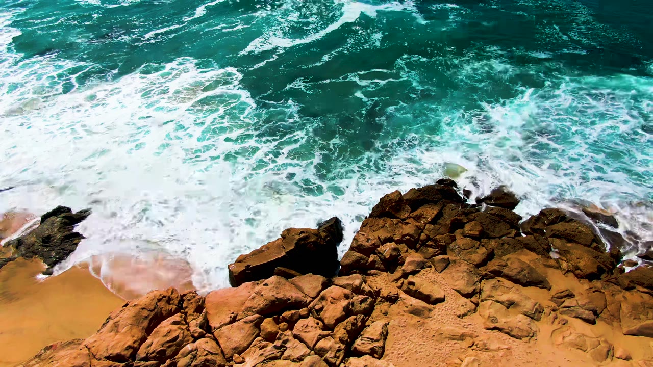 Overhead surf breaking across rocks and orange sand