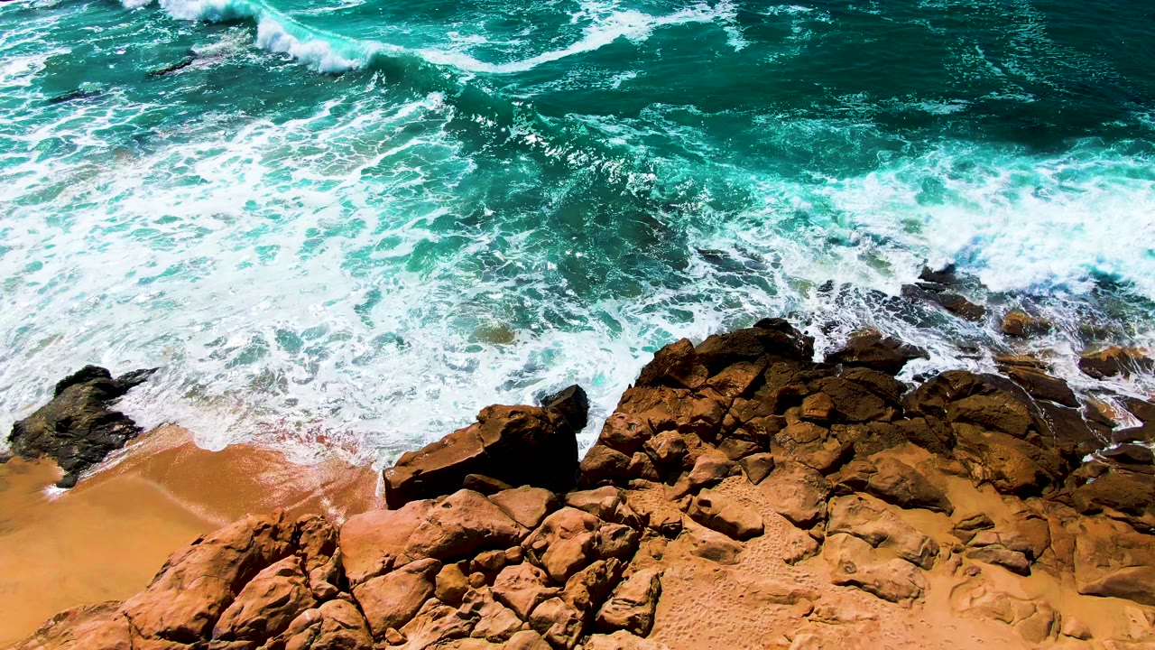 Foam spreads across the midframe as ocean water covers parts of the rocks and beach at Buzzards Beach in Baja California Sur, with no visible people.