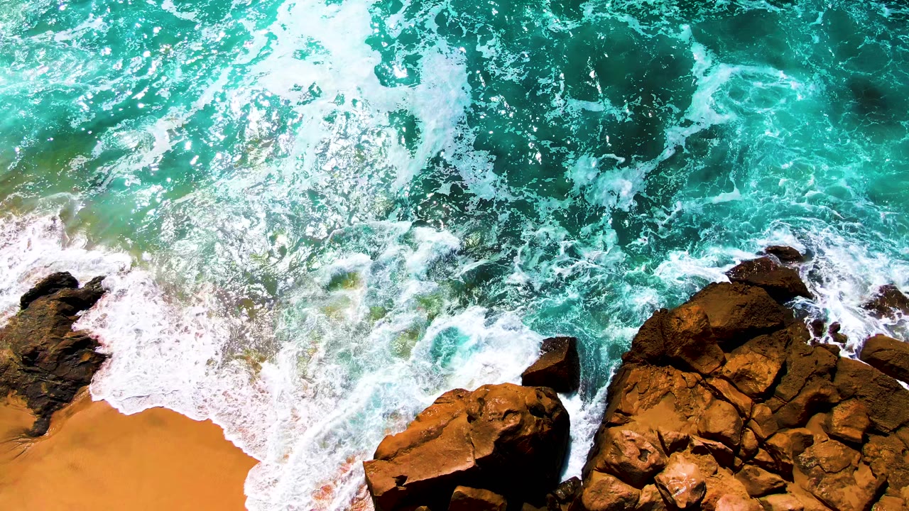 White waves wash around a large rocky outcrop.
