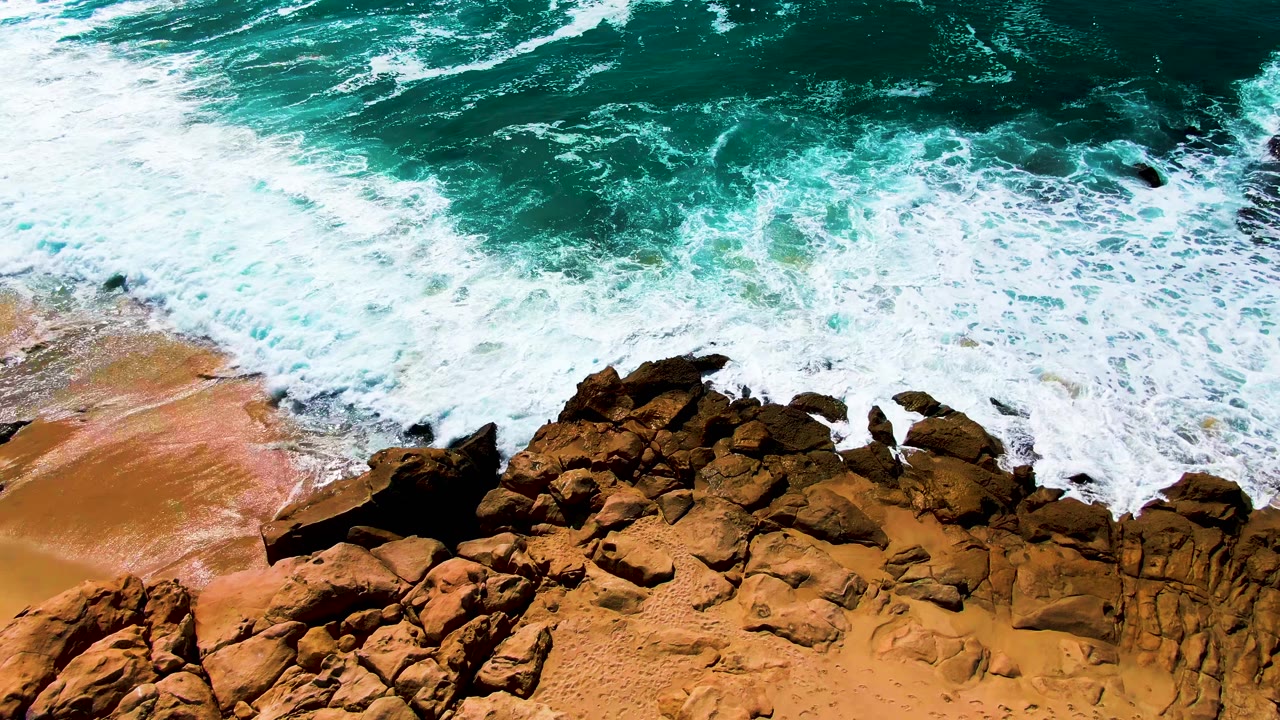 Turquoise surf breaking over rocks and tan sand