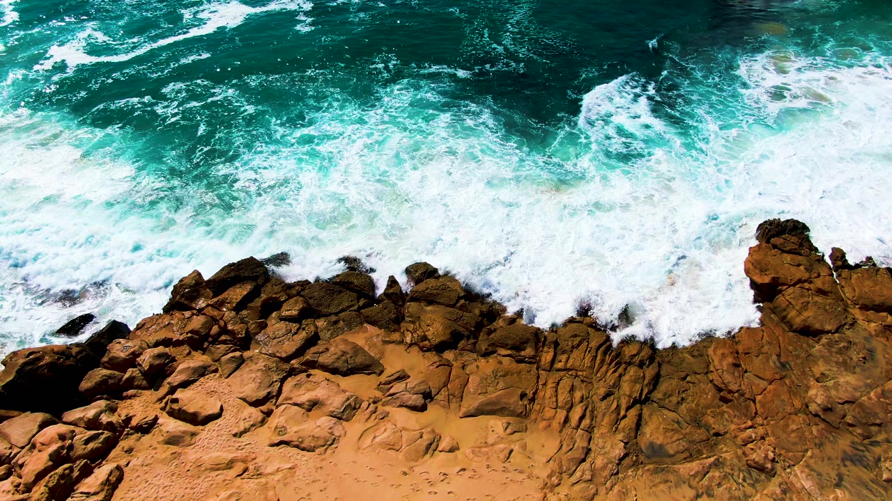 Large white wave wash covers rocks along the coast.