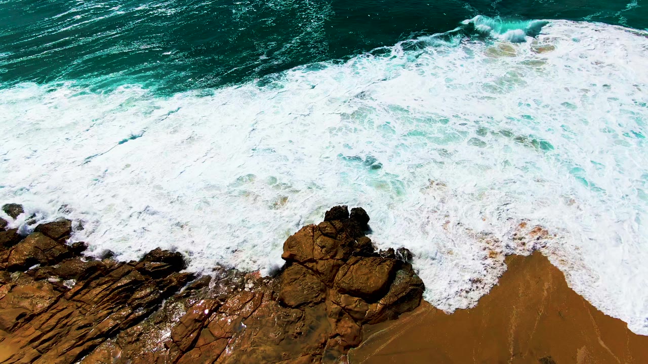 Foam spreading over shoreline rocks from above
