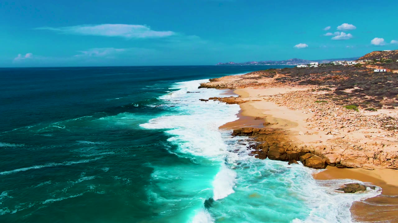 Punta Buzzards coastline seen from above, with bright white foam spreading over turquoise water near shoreline rocks and no visible people.