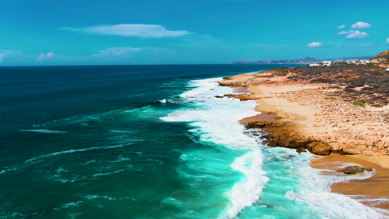 Wide aerial surf view with ocean, white foam, rocks, and sandy beach