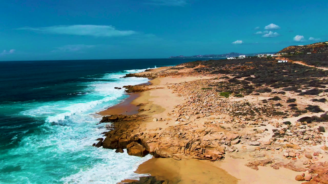 Aerial coastline with turquoise surf curling around rocks and sand.