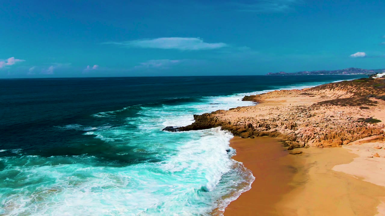 Foamy surf covers shallow water near a tan beach and rocks.