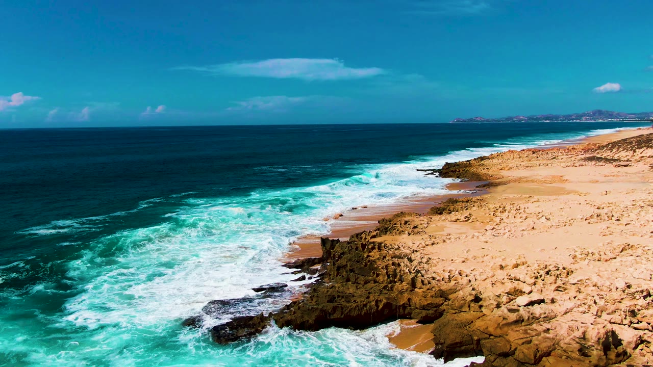 At Punta Buzzards, breaking turquoise water wraps around a dark rocky point beside a wide sandy shore, with no visible people.