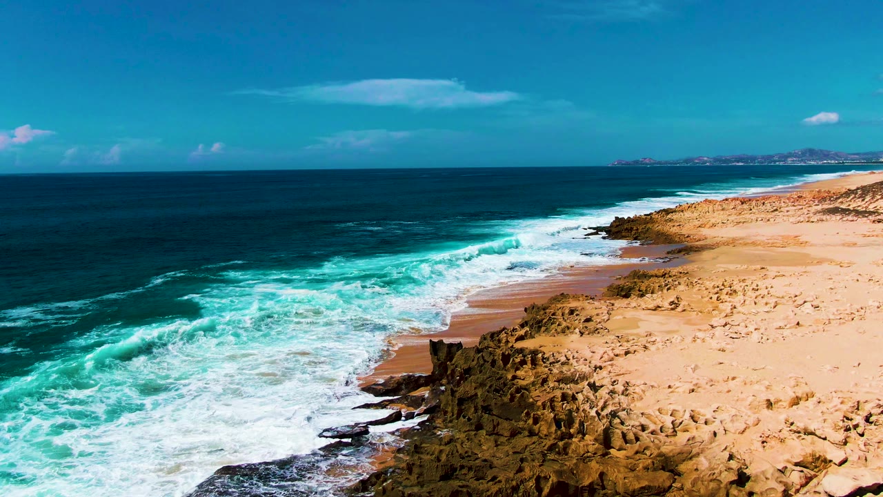 Aerial coastline view with surf sliding along a sandy beach.