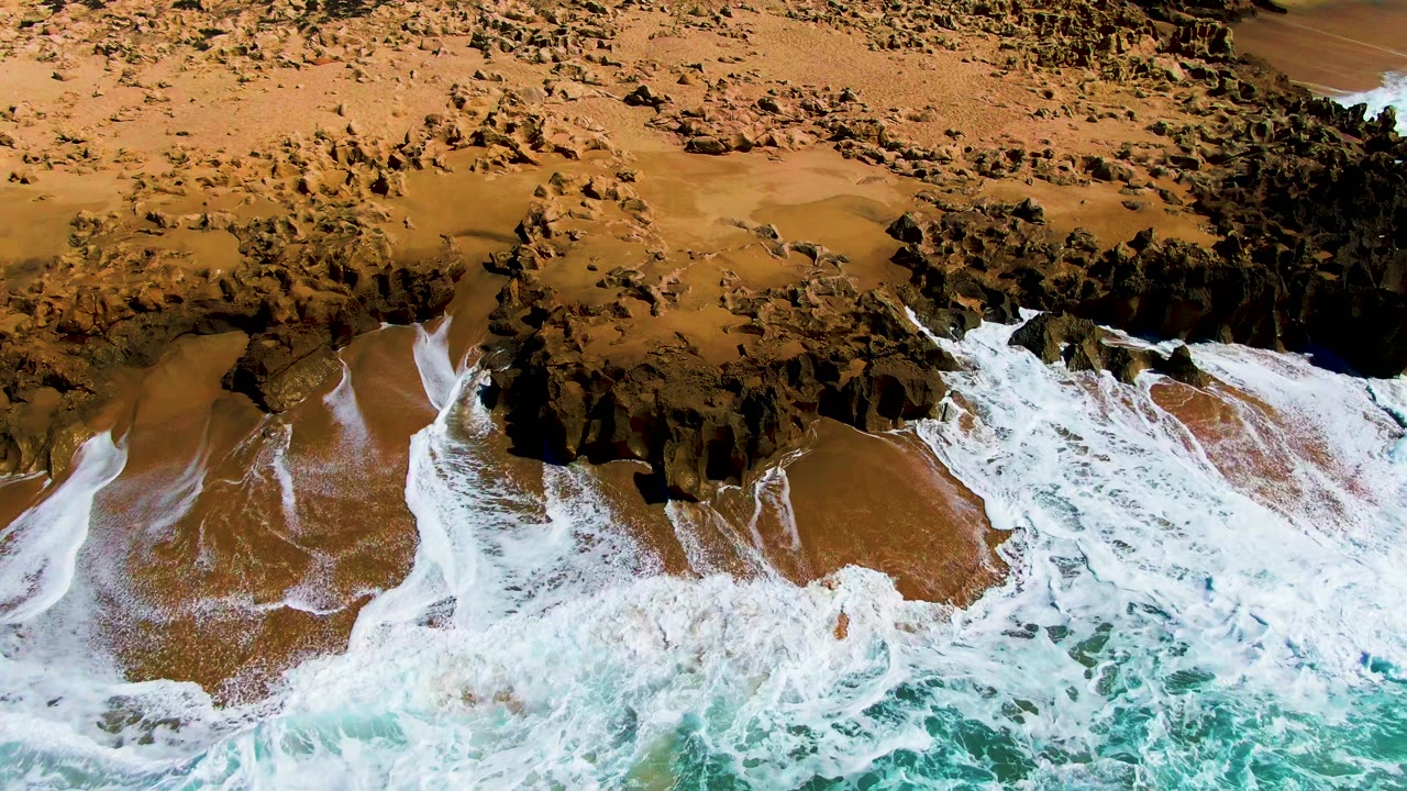 Foam receding across sand beside a rocky outcrop.