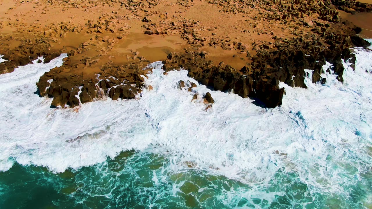 Aerial surf breaking over rocks and sand
