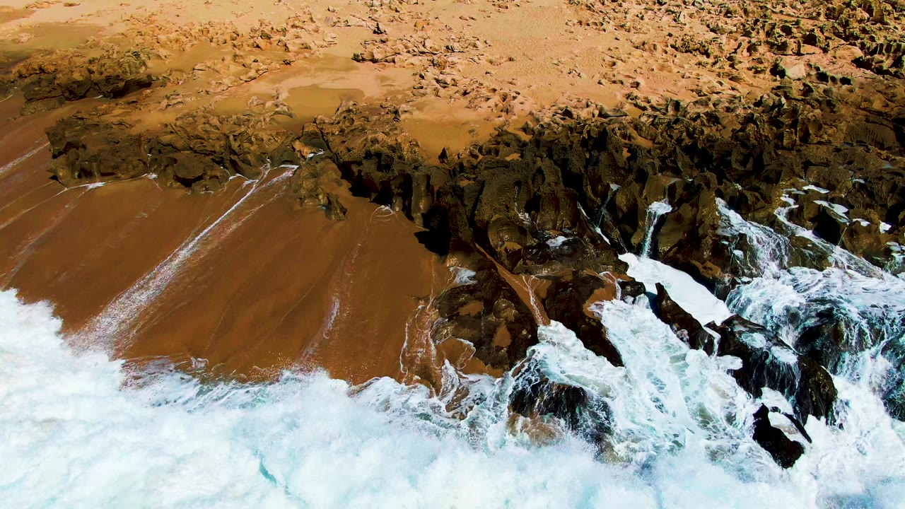 Breaking waves cover part of the sandy beach and rock ledge.