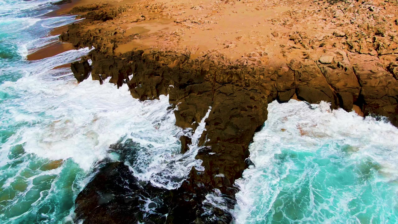 Foamy water covers the lower rocks as waves continue into the cliff.