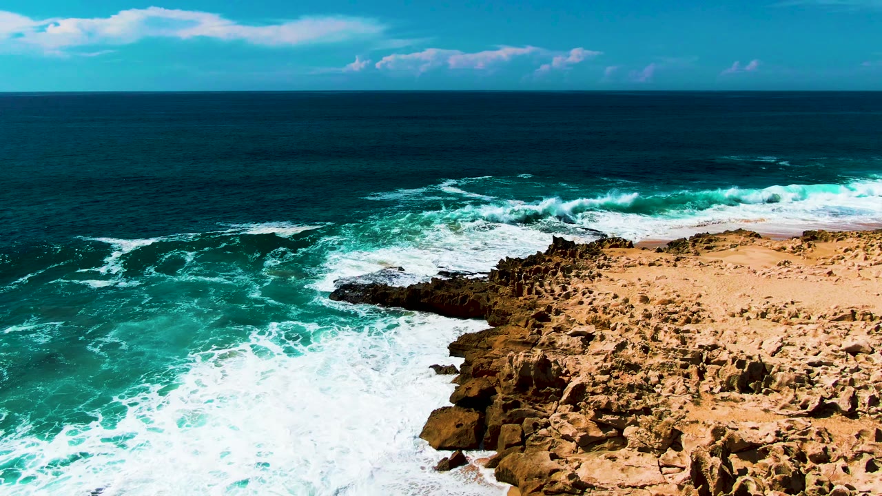 Aerial view of flat rocky coastal shelf with turquoise ocean and blue sky with clouds visible at top of frame