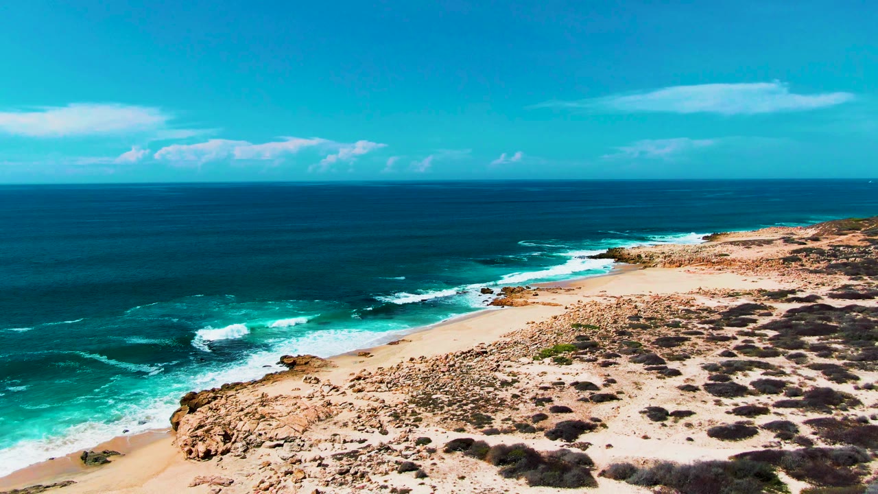 Wide aerial coastline with waves breaking along a pale sandy shore.