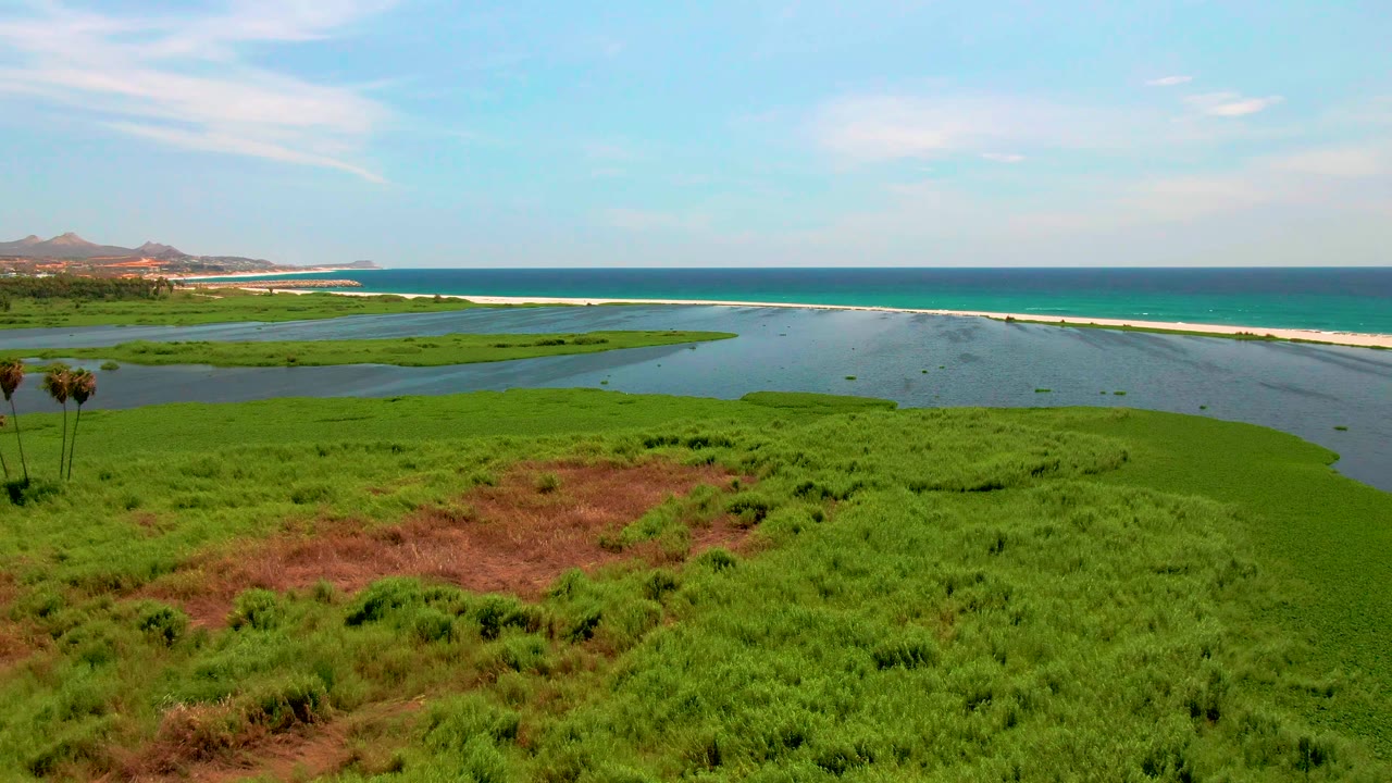 Coastal wetland lagoon with grass, sandbar, ocean, and distant hills.