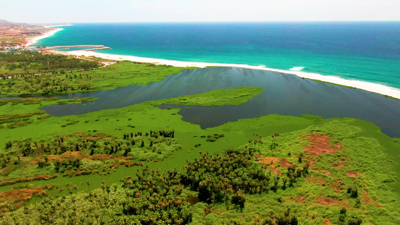 Aerial view of a green lagoon beside a white beach and turquoise ocean.