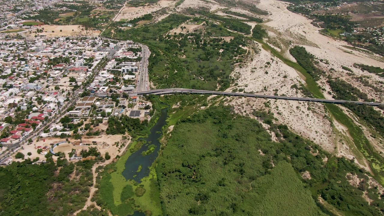 San Jose Del Cabo aerial frame showing light vehicle traffic on the bridge, dense green vegetation below, compact residential blocks, and no visible people.