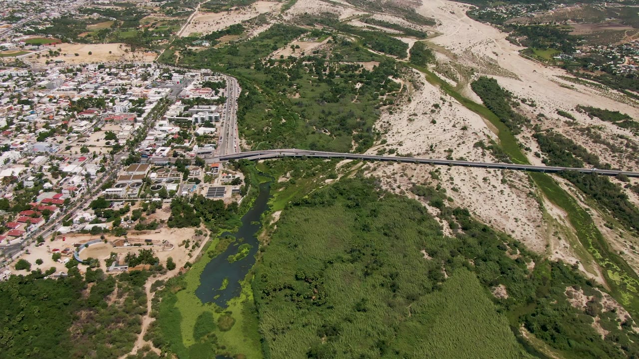 Wide aerial view of road bridge crossing a green river near homes and hills.