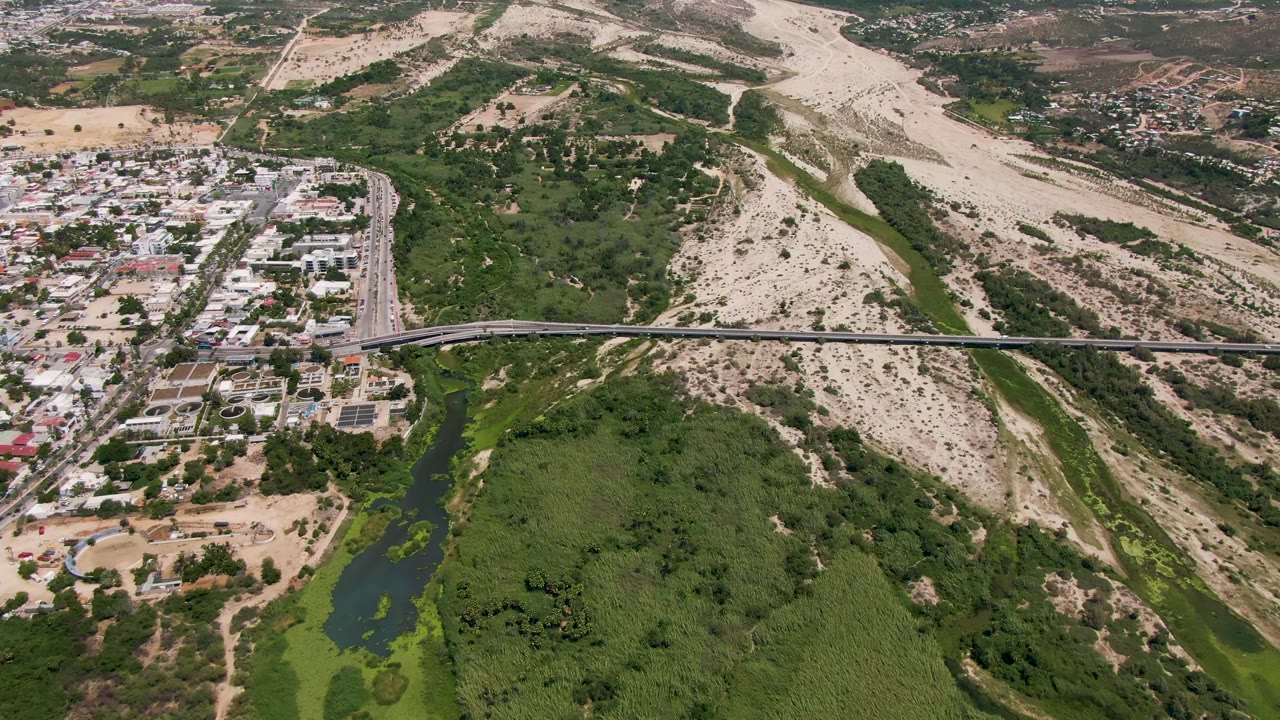 At 0:01, the aerial view holds on traffic along the bridge and road in San Jose Del Cabo, with river greenery below and no visible people.
