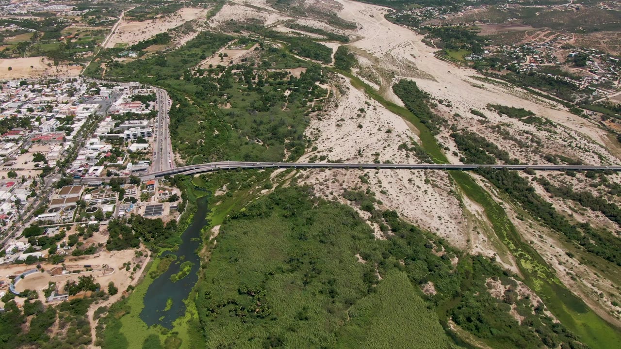 Drone view of bridge traffic over a river with green vegetation and dry hills.