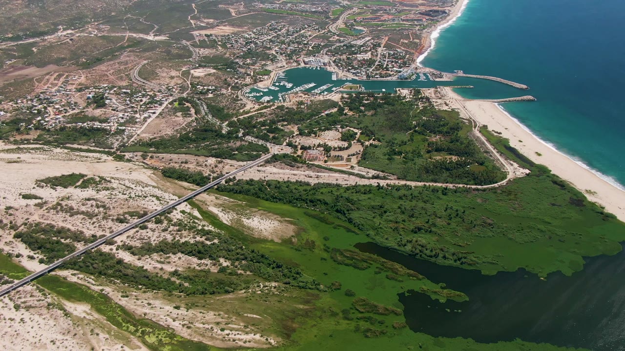 Aerial coastline with bridge over sandy terrain, lagoon, marina, town, and ocean.