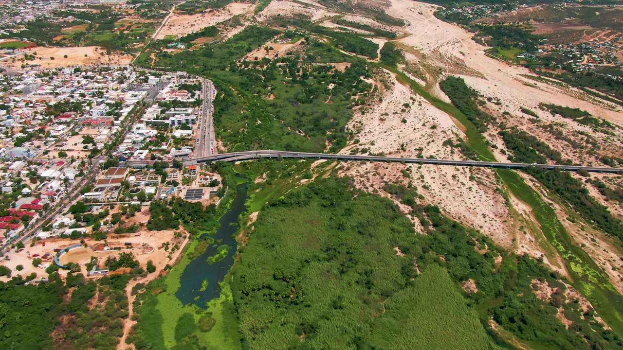 Aerial shot of a bridge across vegetation with residential streets on one side and dry hills beyond.