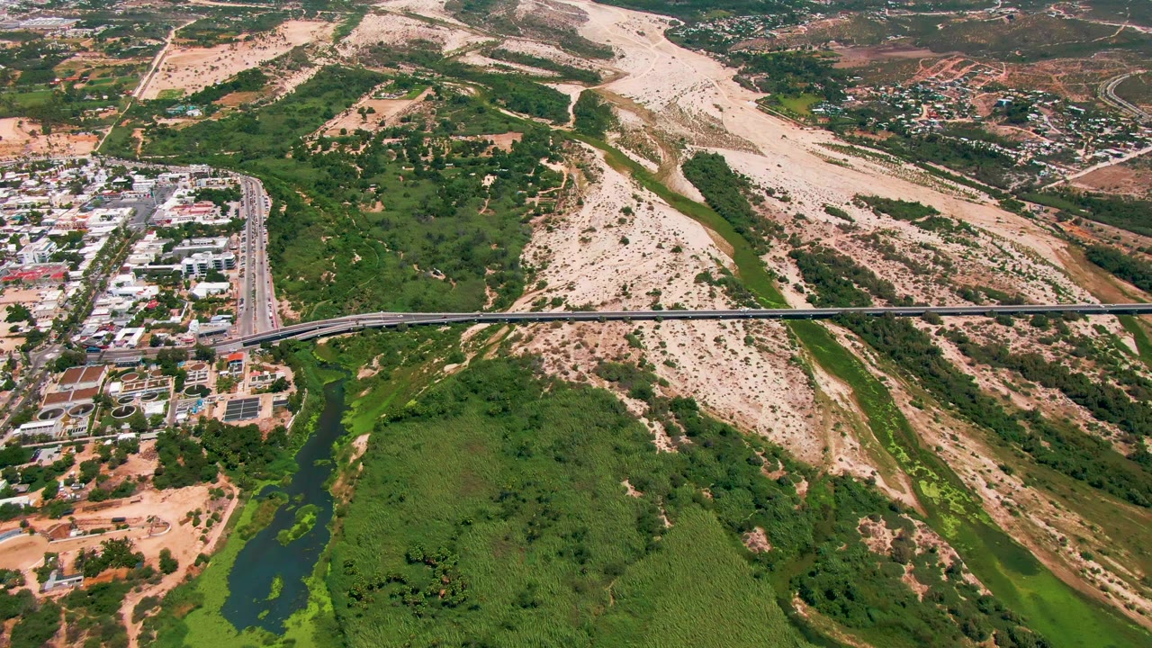 Aerial bridge view with urban buildings on the left and dry hilly terrain filling more of the frame.