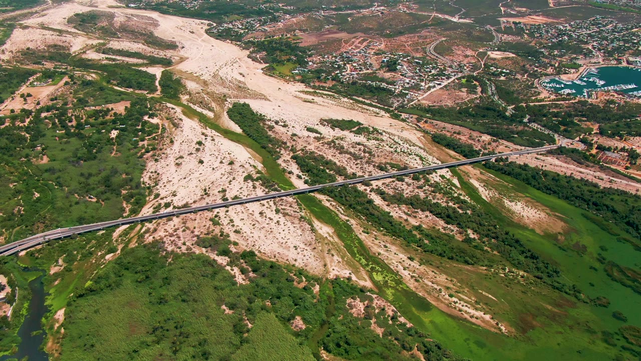 Aerial view of a bridge crossing a green river channel and pale riverbed.