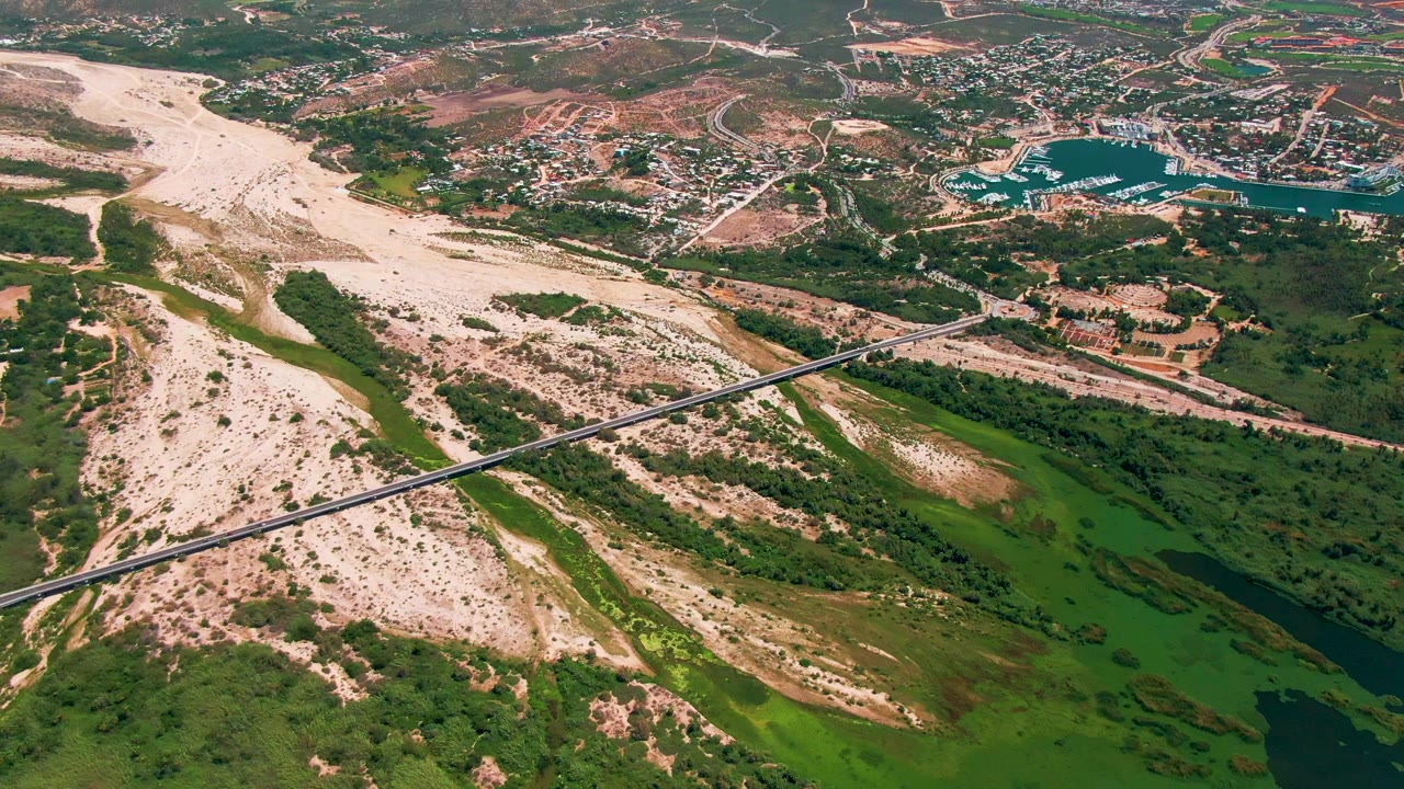 Aerial view of sandy coastal wash, bridge, green vegetation, and town beyond.