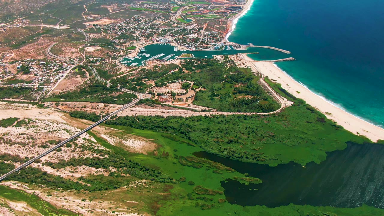 Wide aerial of marina entrance, beach, roads, green lagoon, and blue ocean.