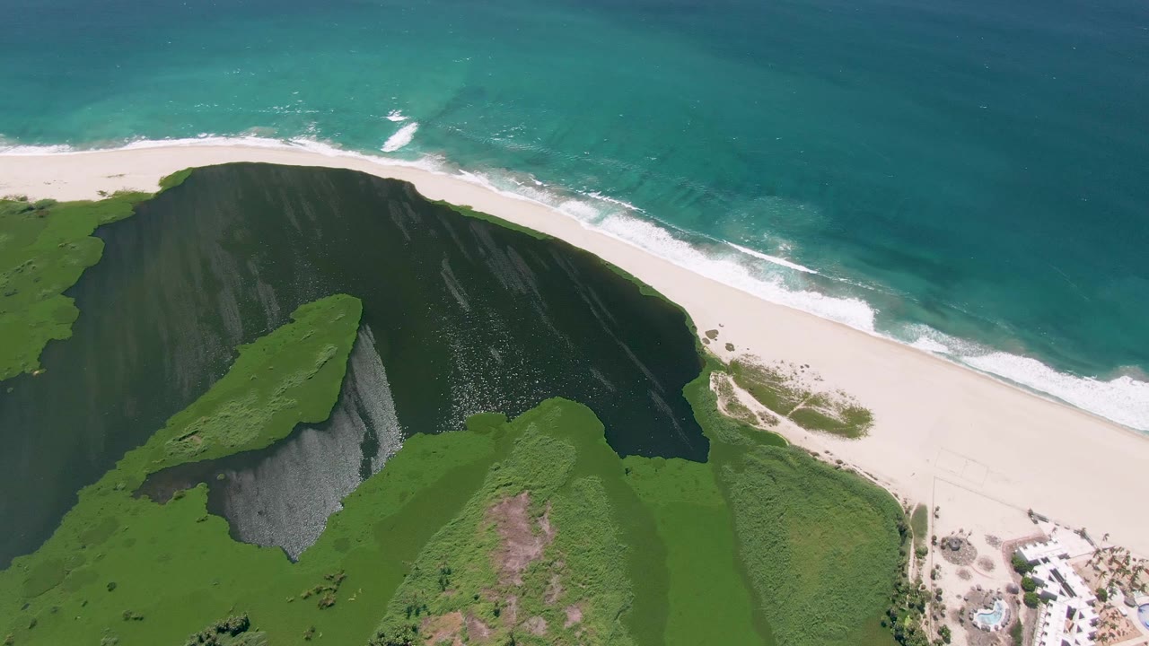 Aerial view of green cliffs, white sand beach, and turquoise ocean.