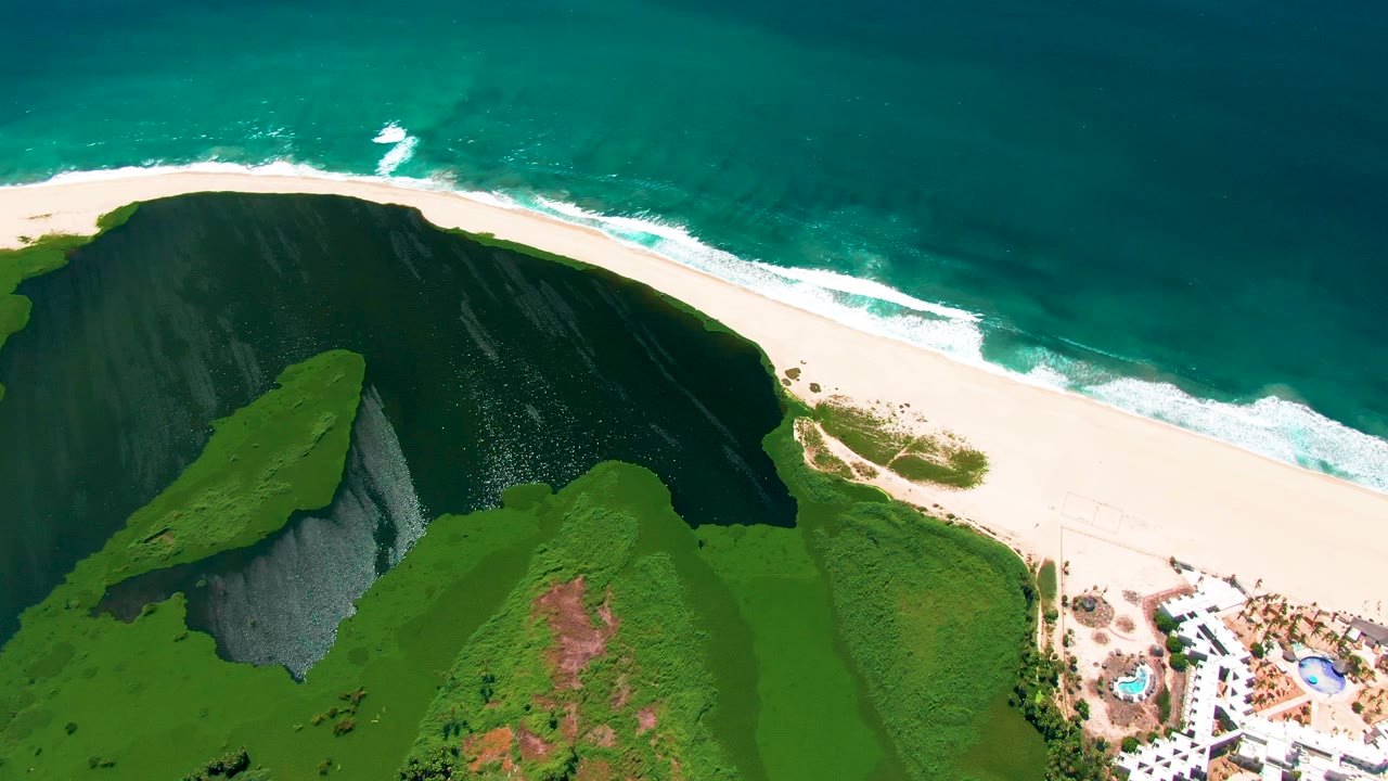 Aerial view of green cliff, white beach, turquoise ocean, and resort buildings.