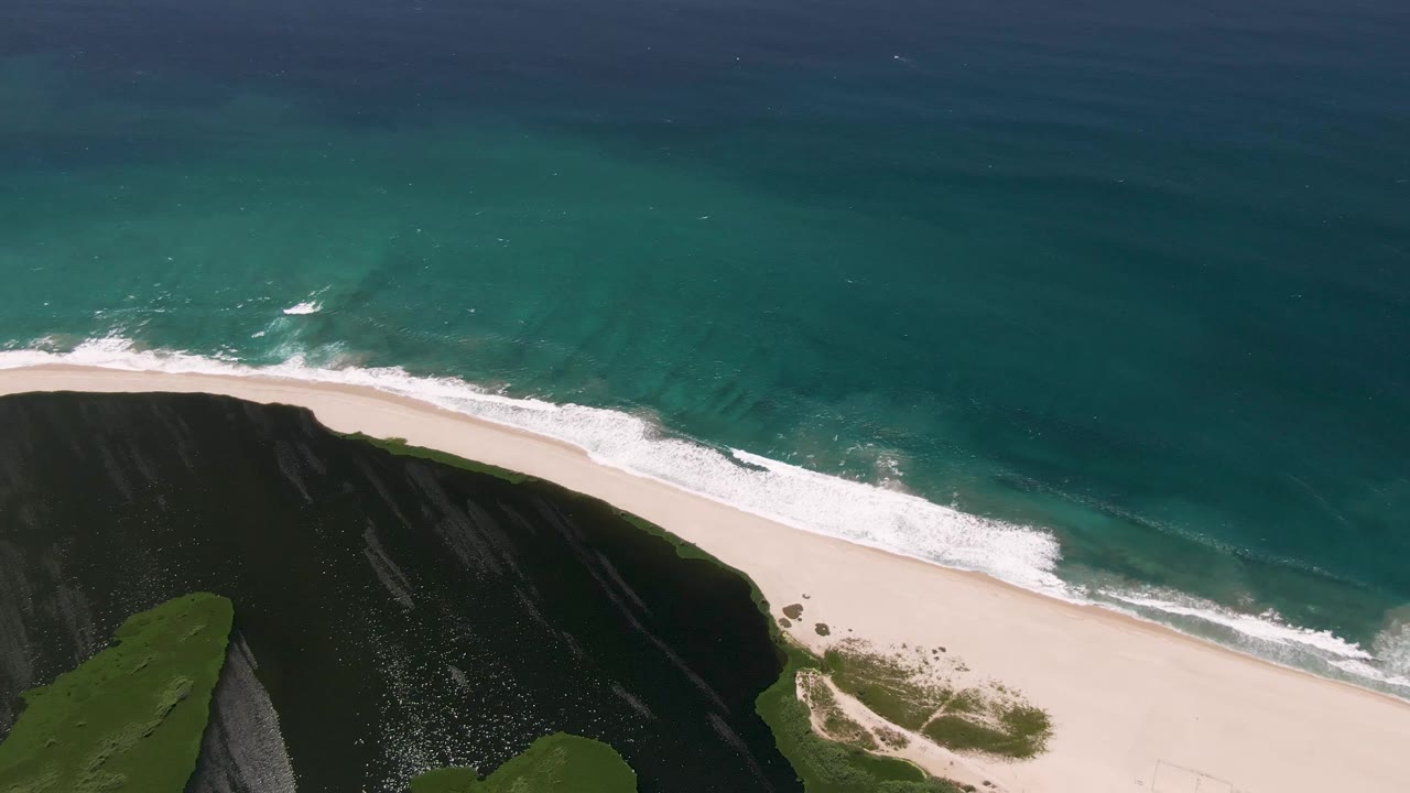 At 0:03, the San Jose del Cabo beach sits between dark cliff terrain at the bottom edge and broad turquoise ocean above, with no visible people or structures.