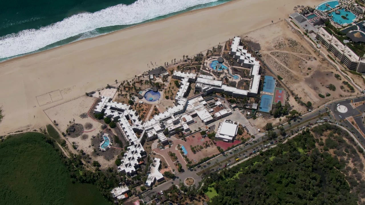 Closer overhead view of the resort with beach, surf, pools, road, and green area.