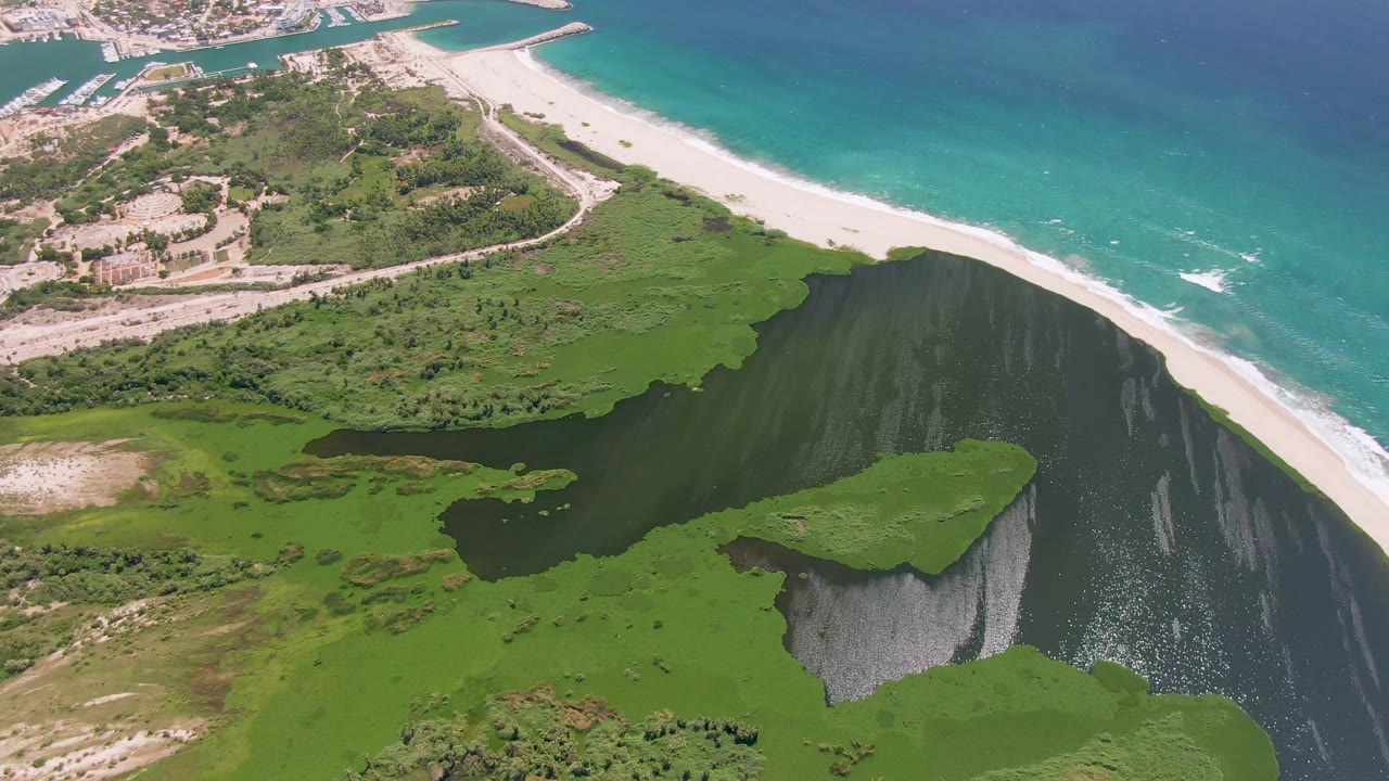 Aerial view of green coastal lagoon beside white sand beach and turquoise ocean.