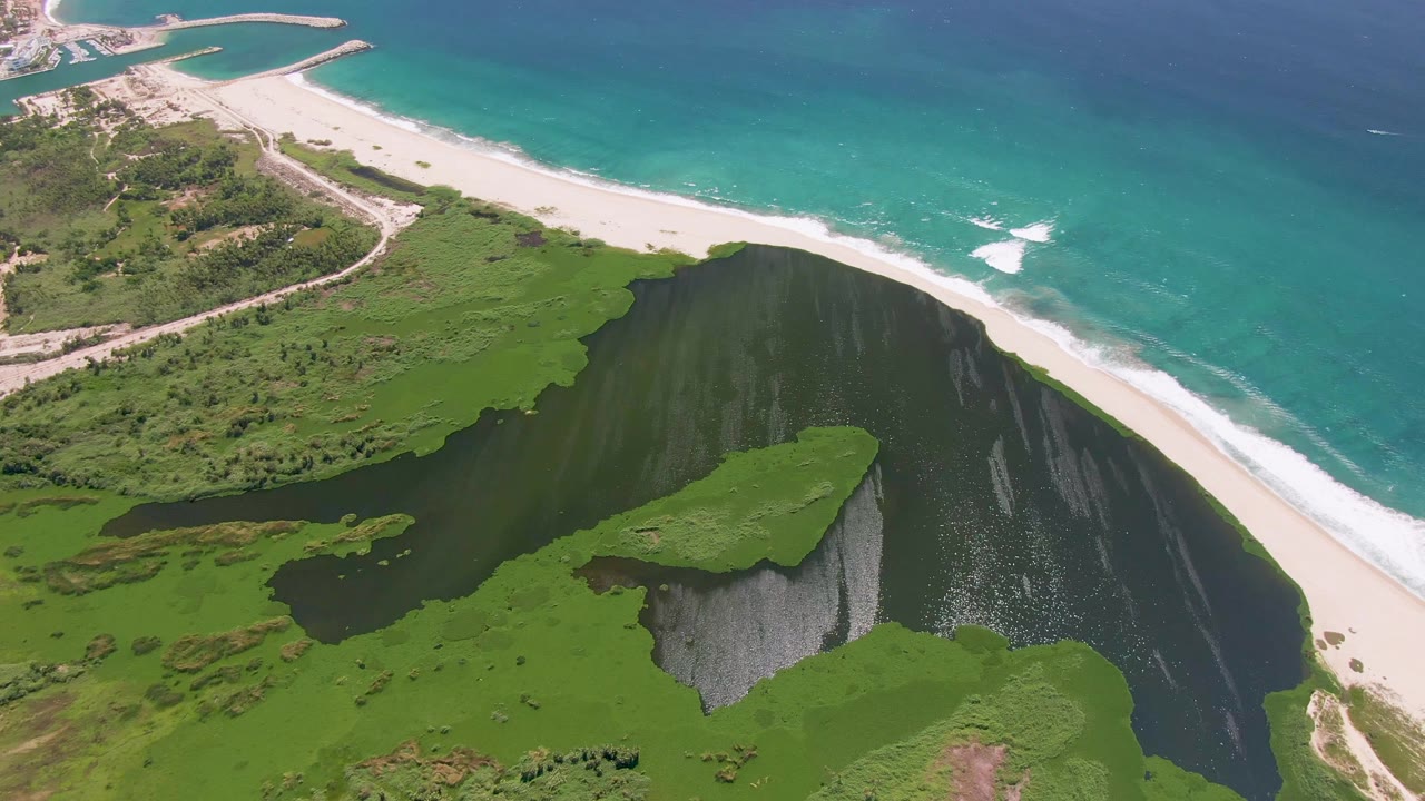 Aerial coastline with a beach between dark lagoon water and blue ocean.