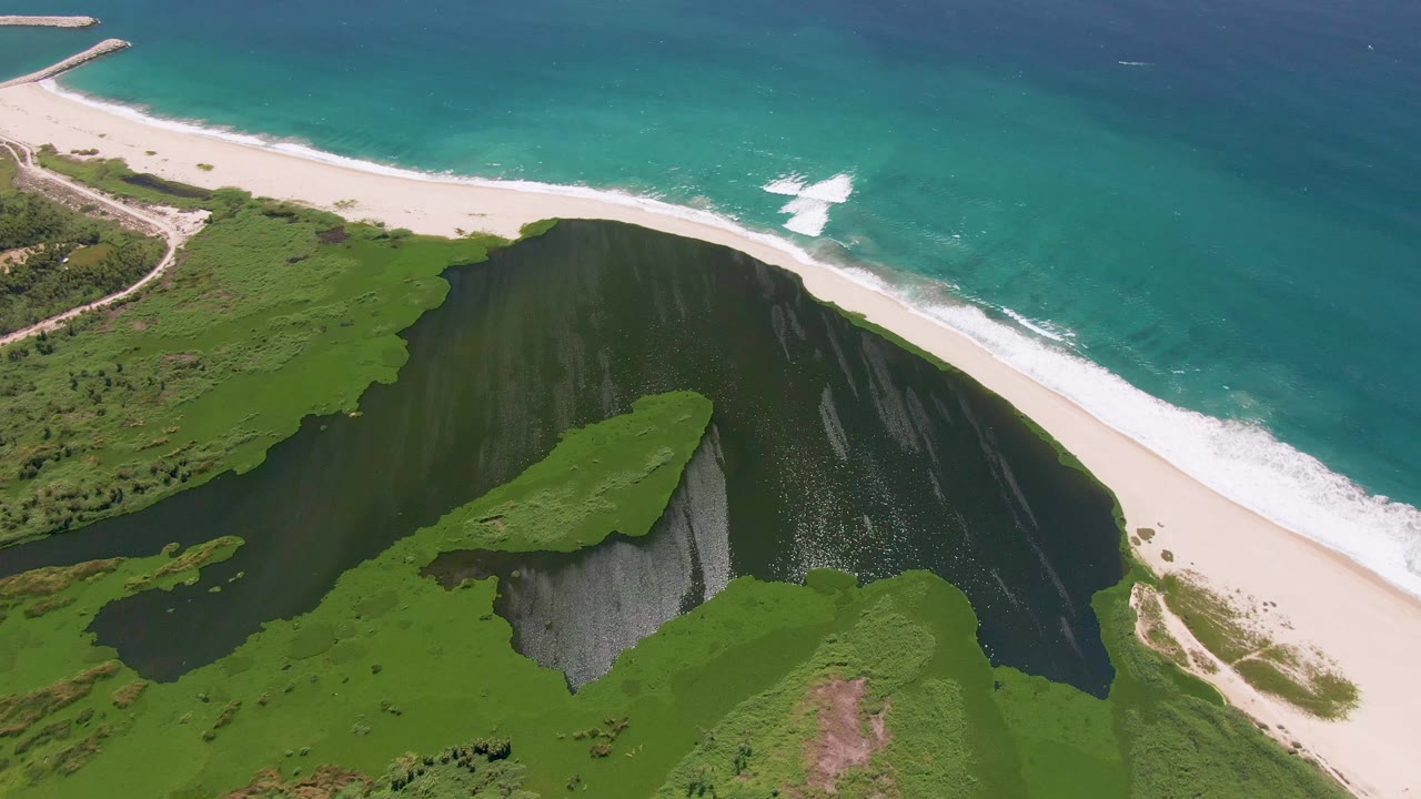 Opening aerial frame over San Jose del Cabo green coastal cliffs, pale sand, turquoise ocean, white surf, and no visible people.