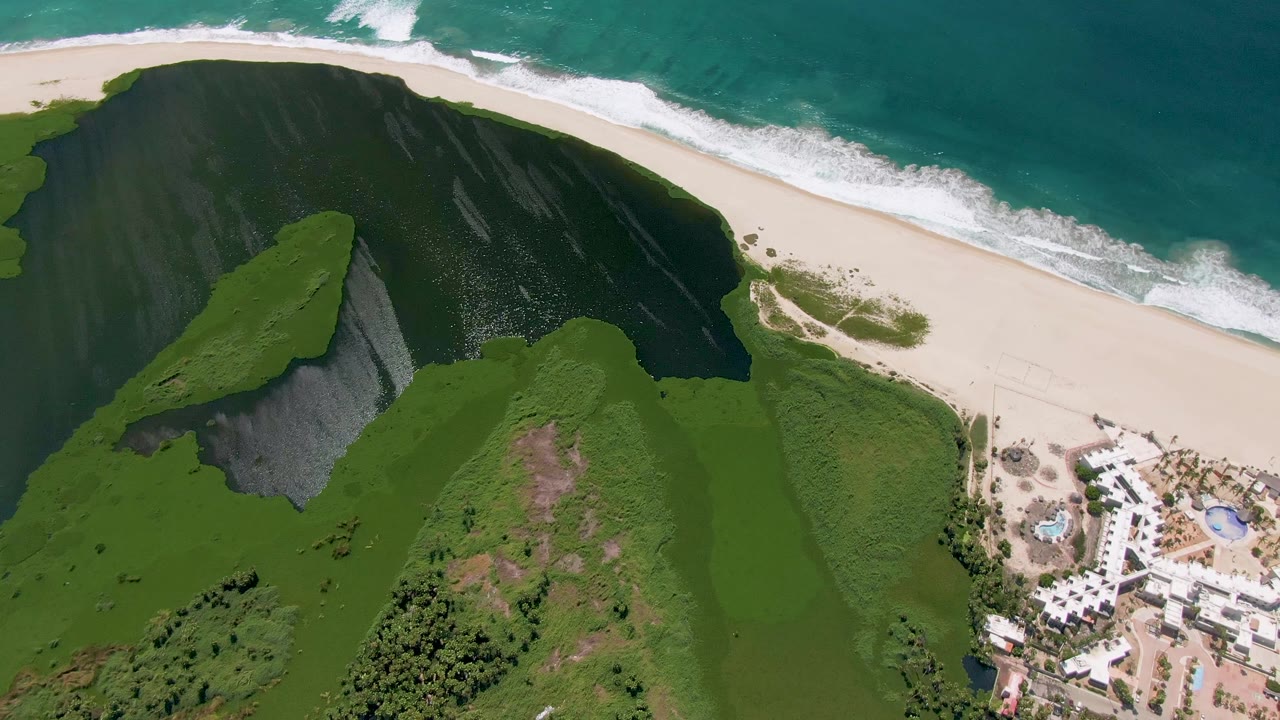 Fourth aerial frame in San Jose del Cabo with the green bluff filling more of the lower frame, the beach and surf across the top, and no visible people.