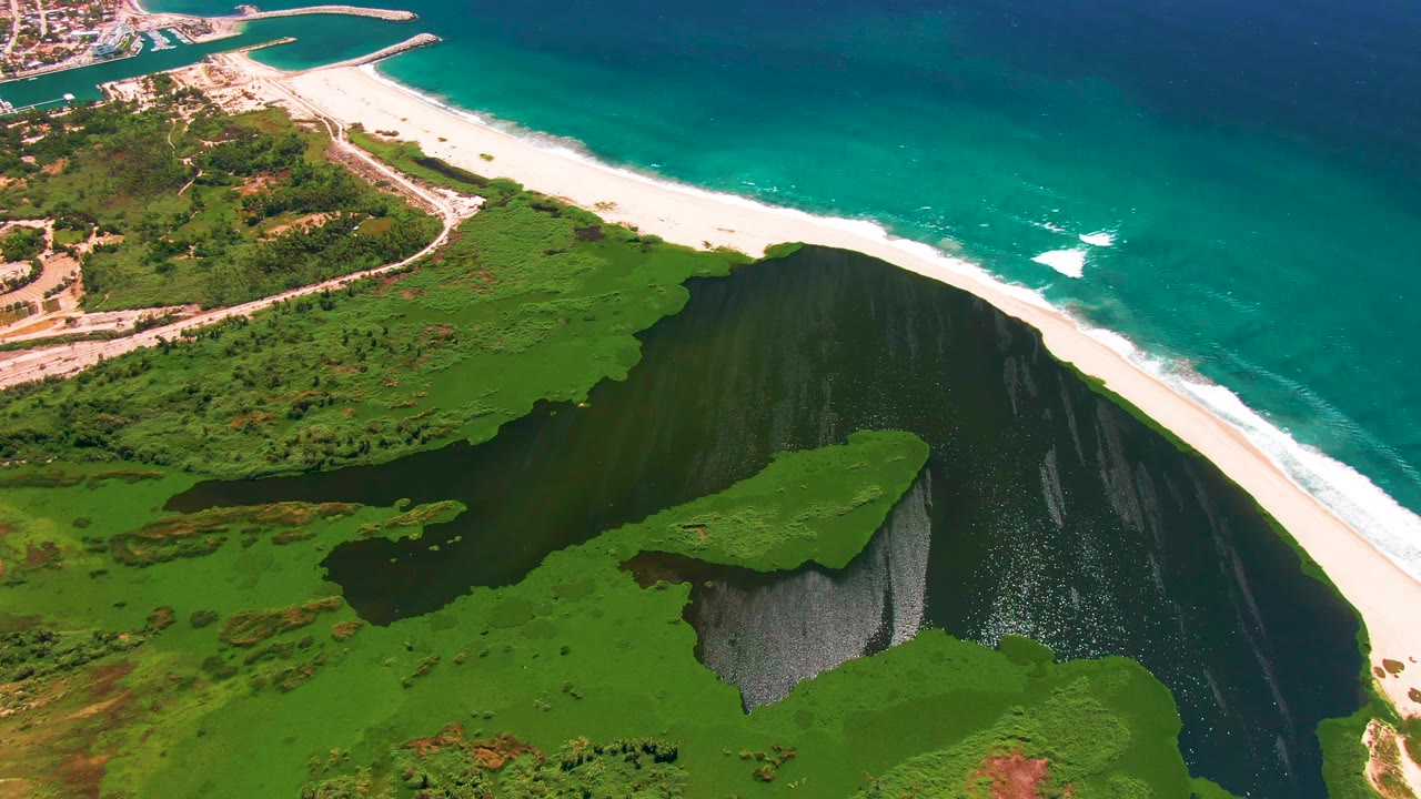 Aerial coastline with lagoon in the foreground and ocean surf along a white beach.