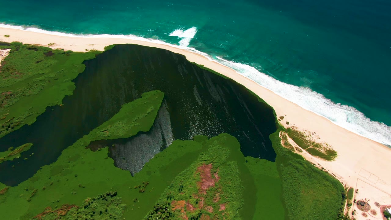 Aerial coastline view with cliff shadow, beach, surf, and ocean.
