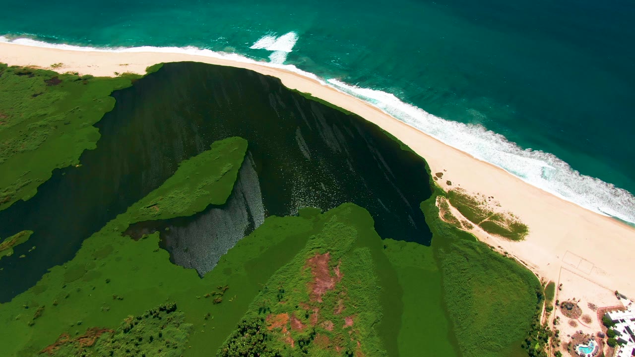 Aerial frame of cliff, bright sand beach, surf, and coastal paths.