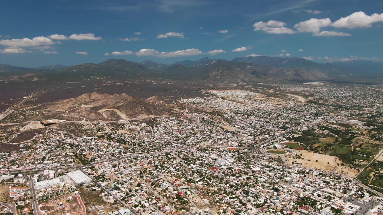 Wide aerial view of dense buildings below hills and a mountain horizon.