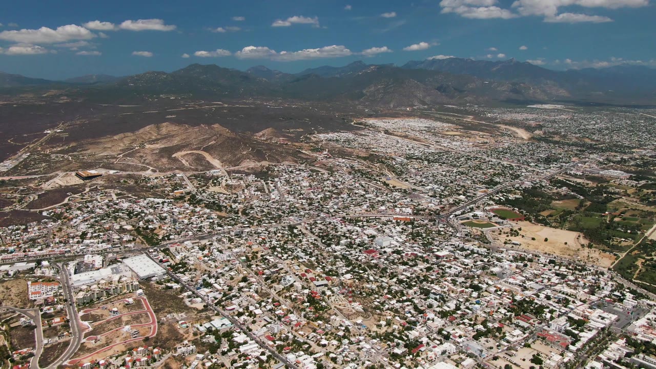 Wide aerial view of white-roofed neighborhoods with mountains beyond.