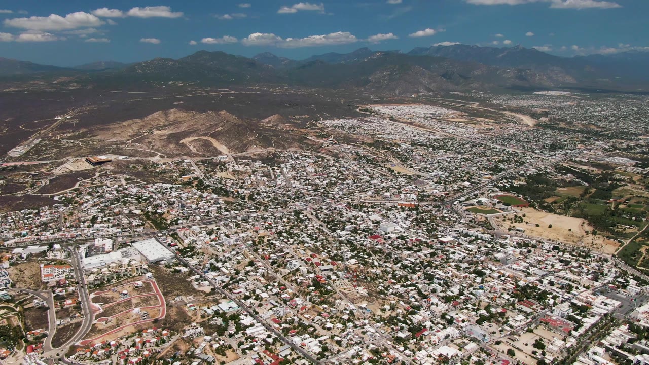 High view across a dense city, hillside cuts, and a broad mountain horizon.