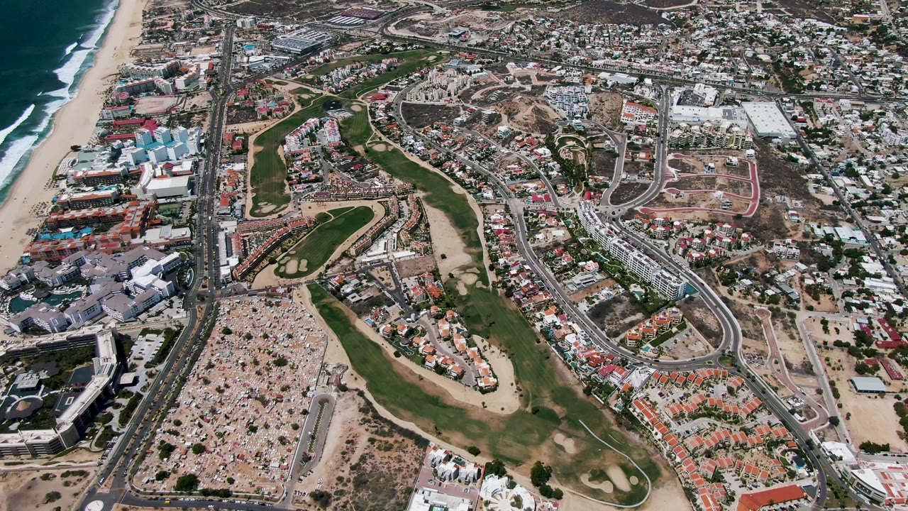 Aerial coastal neighborhood with ocean, sandy beach, golf course, and roads.