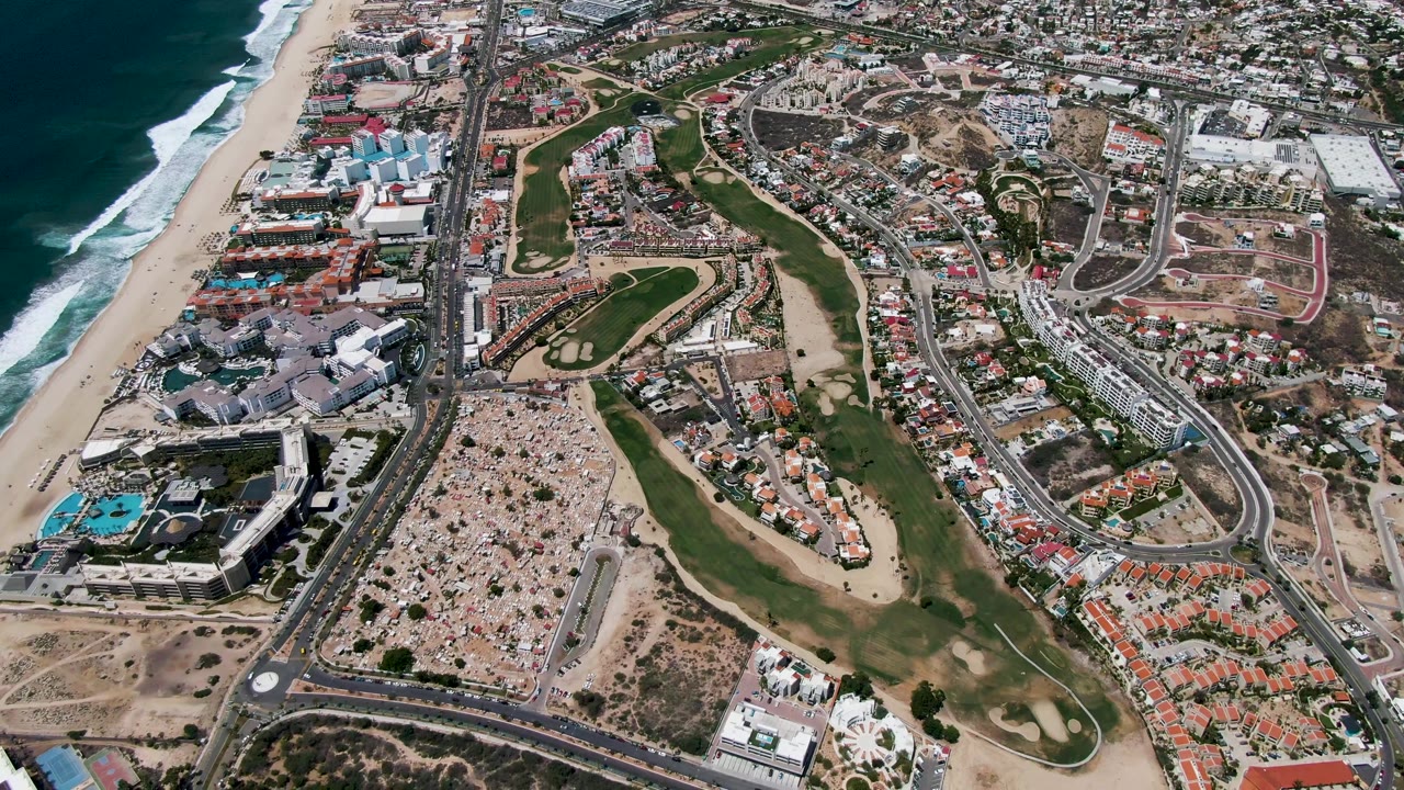 Coastal aerial with resort buildings, highway lanes, golf fairways, and surf.
