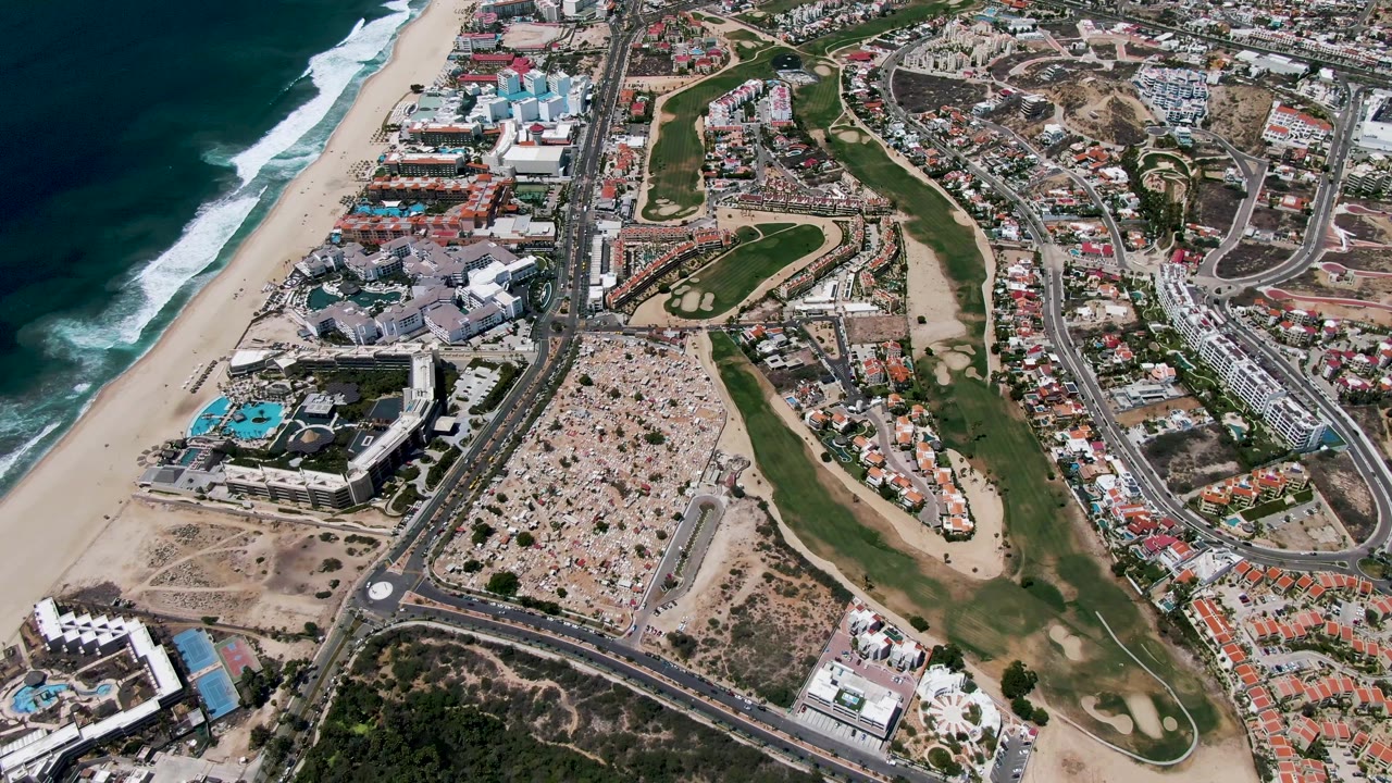 Aerial coastline with beach, resort pools, golf course, roads, and residential blocks.