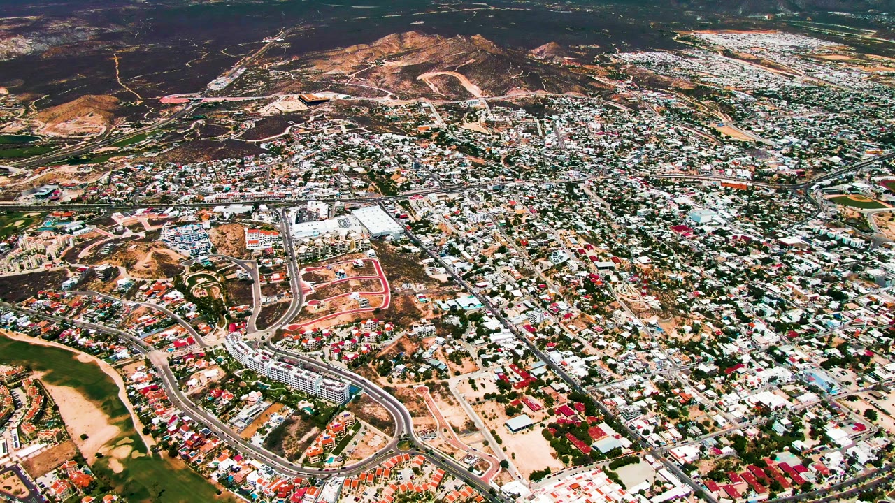 Aerial neighborhood view with winding roads and hillside background.