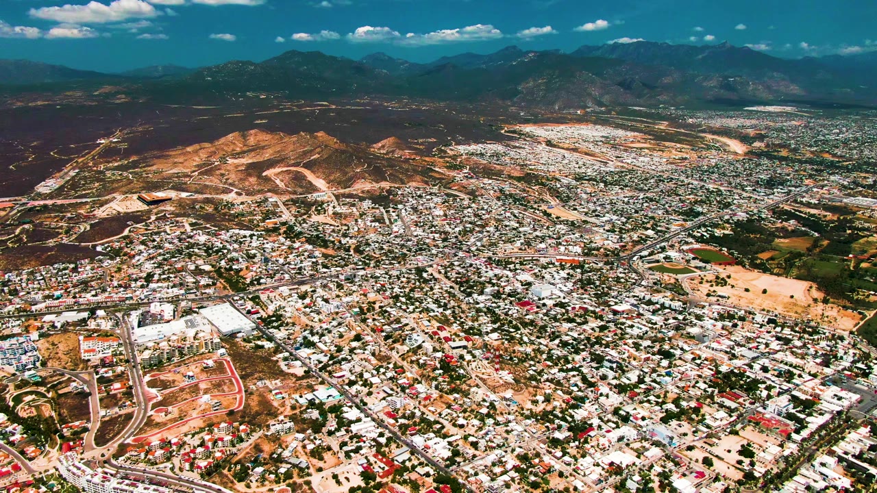 Aerial view across dense buildings toward brown hills and mountains.
